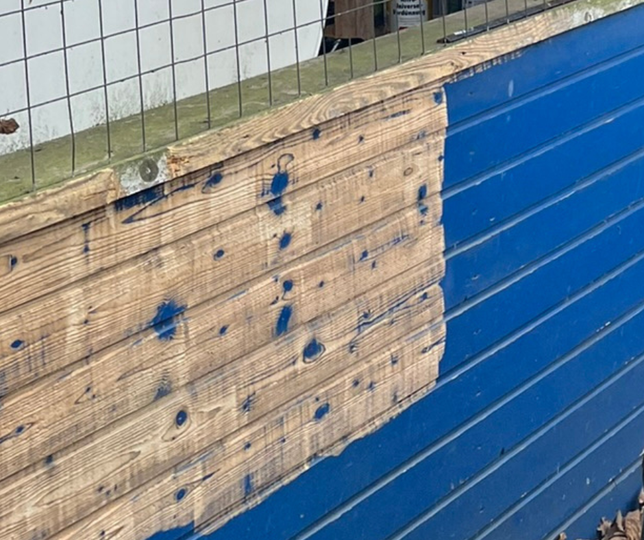 Eine blaue Holzwand wurde auf einer Hälfte mit Trockeneisstrahlen gereinigt und ist nun wieder unlackiert.